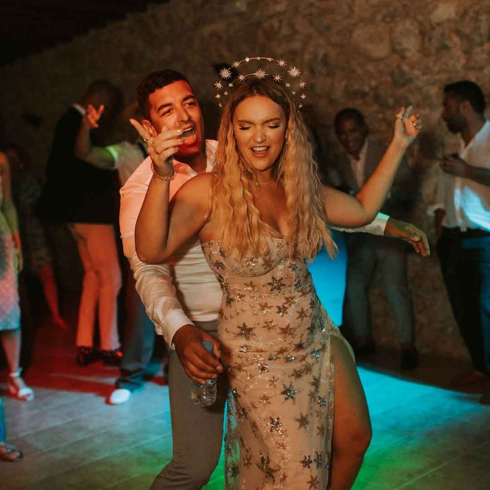 Bride in sleeveless front slit celestial wedding dress and ethereal gemstone bridal crown dancing with groom in white shirt and grey trousers 