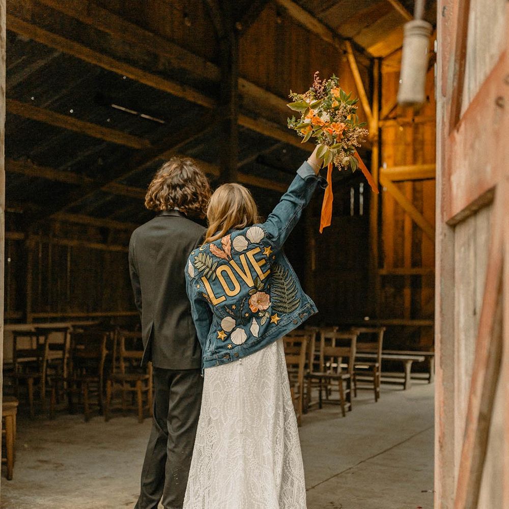 Bride in embroidered 'LOVE' motif denim jacket for rustic barn wedding 