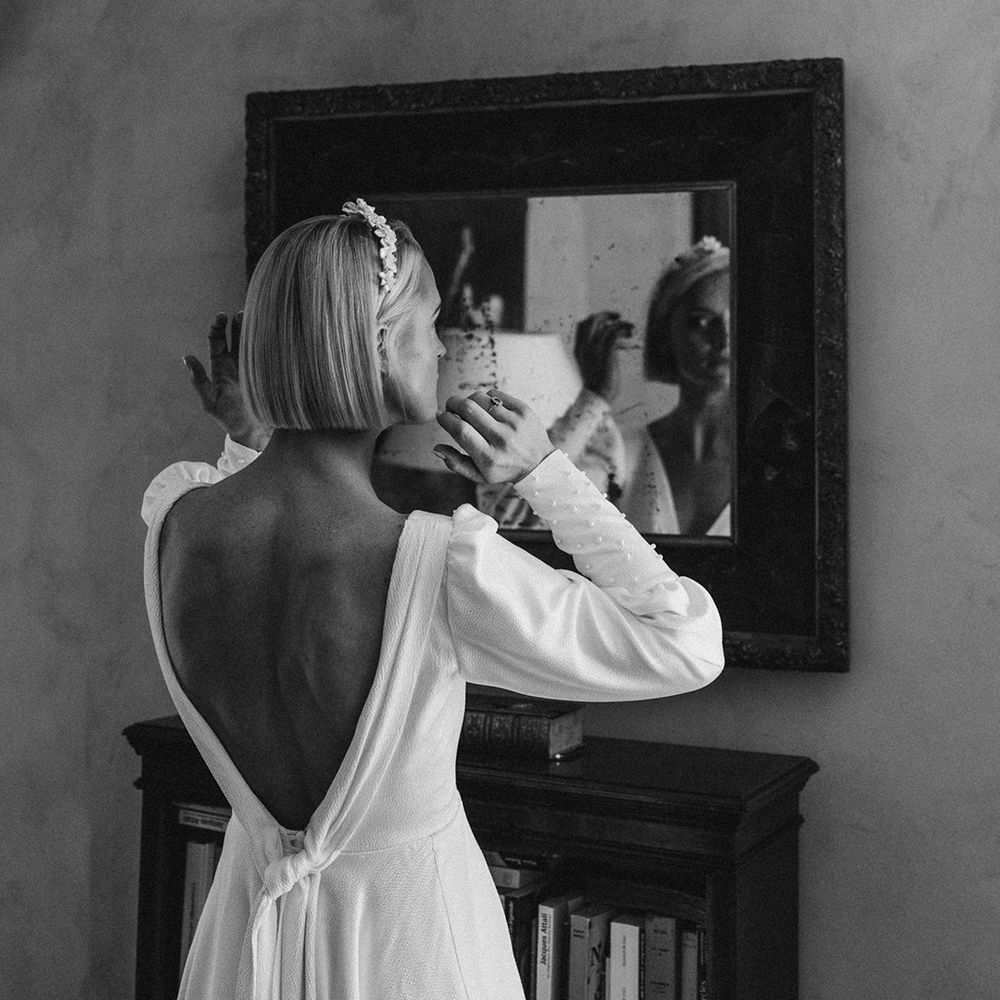 bride with short bob hair and low back wedding dress looking at herself in the mirror on the wedding morning 