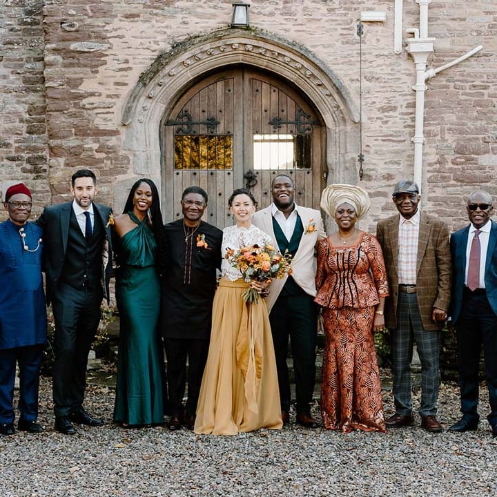 Wedding party standing with bride in white mesh lace bridal crop top and yellow wedding skirt holding dried autumnal wedding bouquet with sunflowers, garden roses, pampas grass, eucalyptus, yellow tall kangaroo paws, orange osmanthus flowers, foliage and dried flowers standing outside of Broadfield Court wedding venue