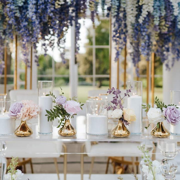 Wedding top table with hurricane vases and pillar candles, gold flower vases, pastel flower centrepieces and pastel and foliage flower arrangements 
