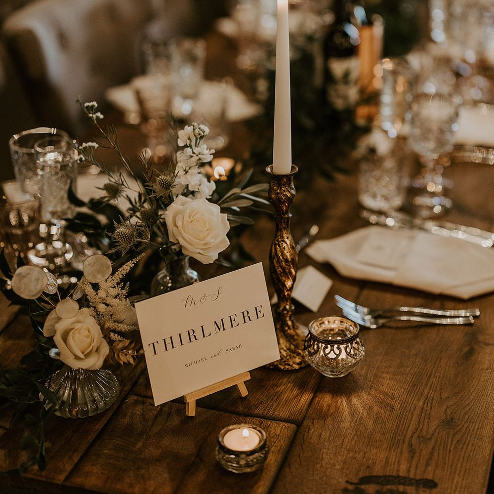 Minimalist and classic black and white wedding table name sign siting next to traditional white wedding flower arrangements for the table 
