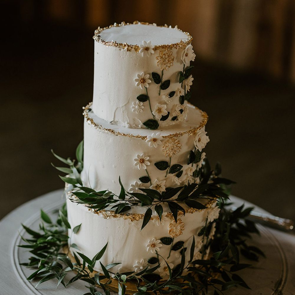 White three tier rustic wedding cake with iced flowers and green foliage 