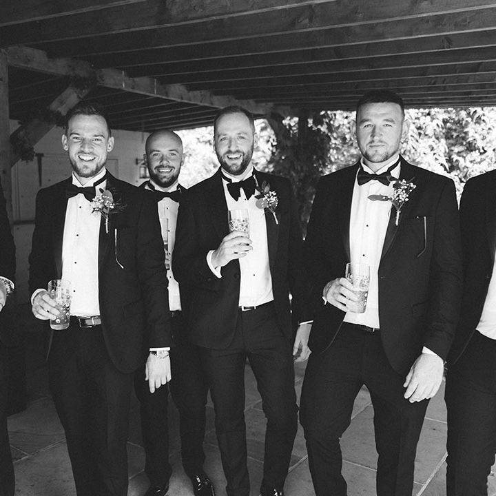 Groomsmen wearing black tie wedding tuxedos with floral buttonhole accessories 
