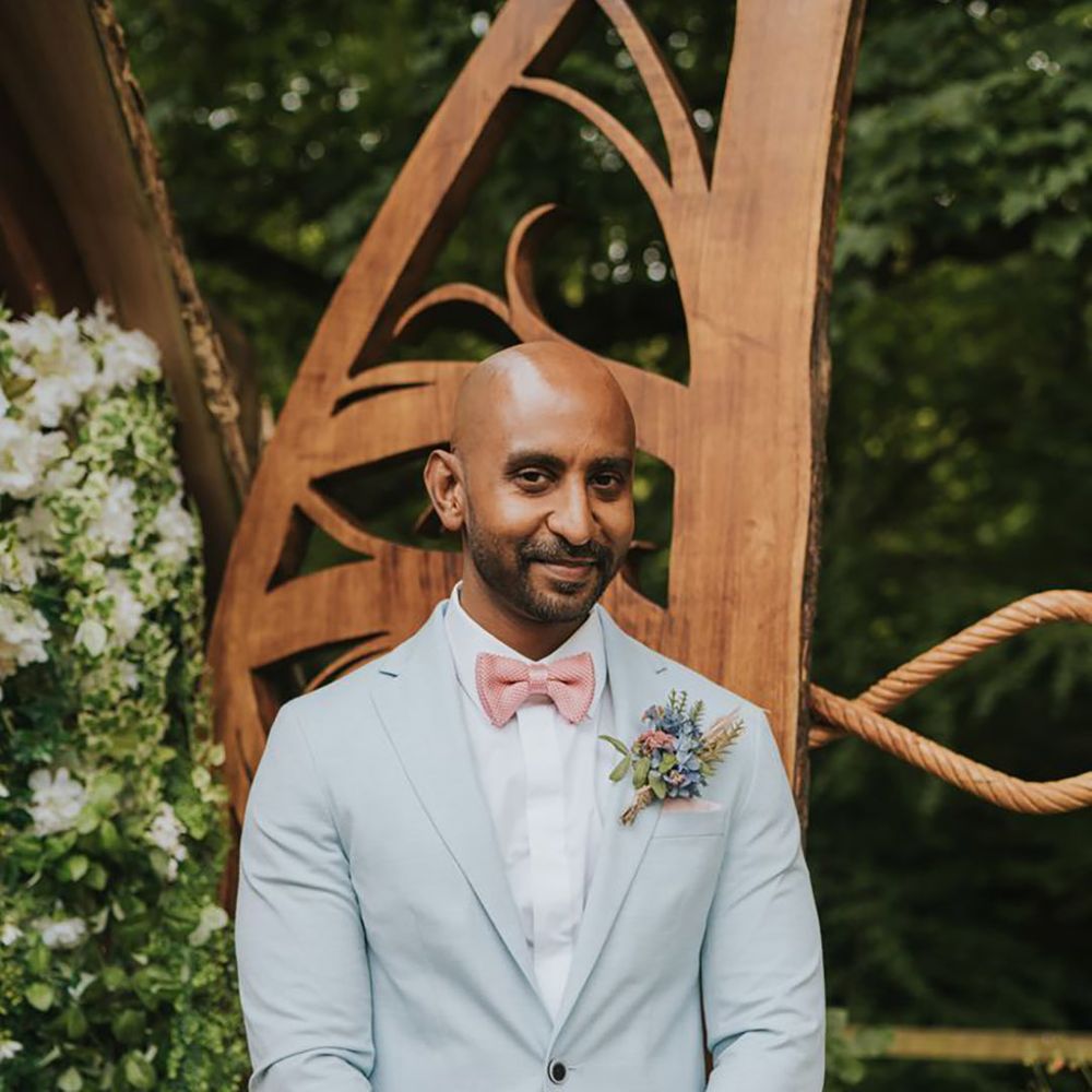 Groom in light blue pale wedding suit with pink bow tie and pocket square with colourful buttonhole 