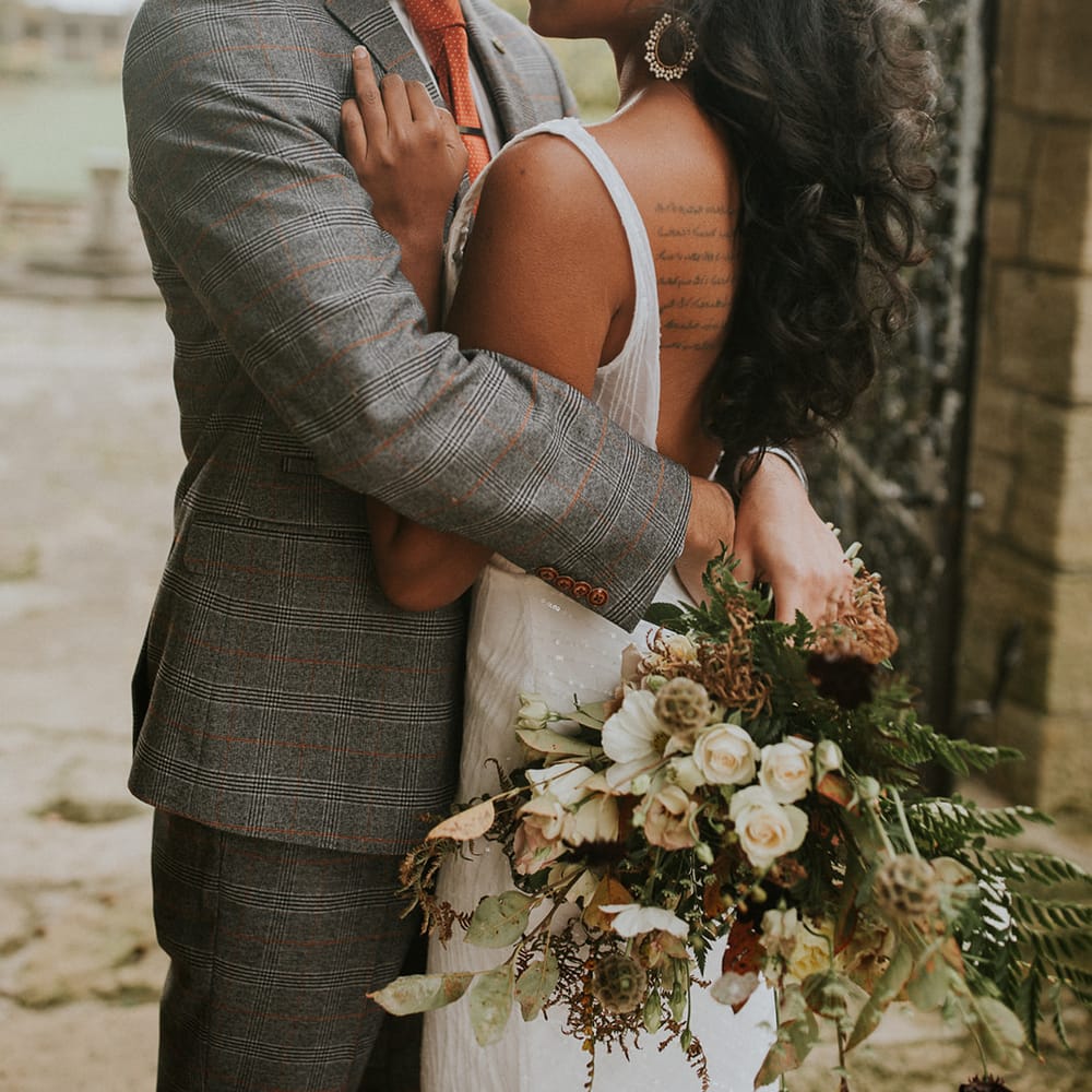 Groom in grey check suit embracing his bride in a low back dress