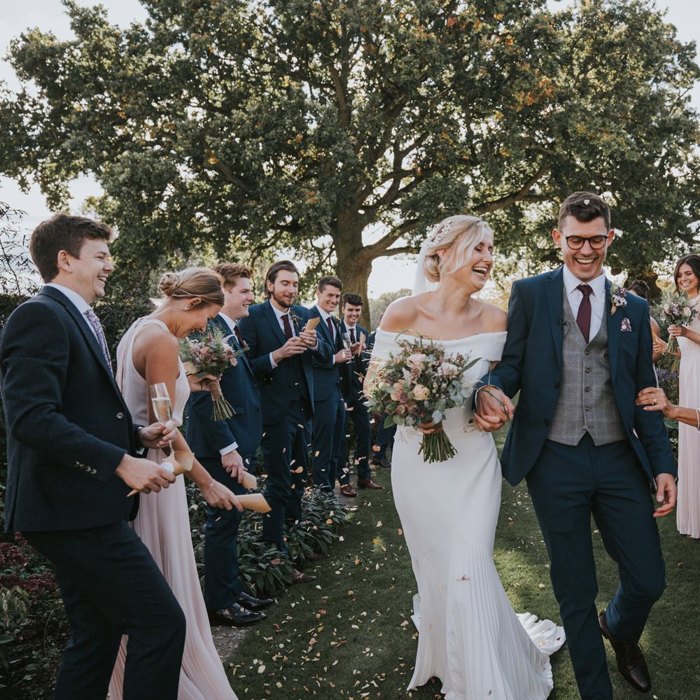 Bride & groom hold hands as they walk through wedding party throwing confetti 