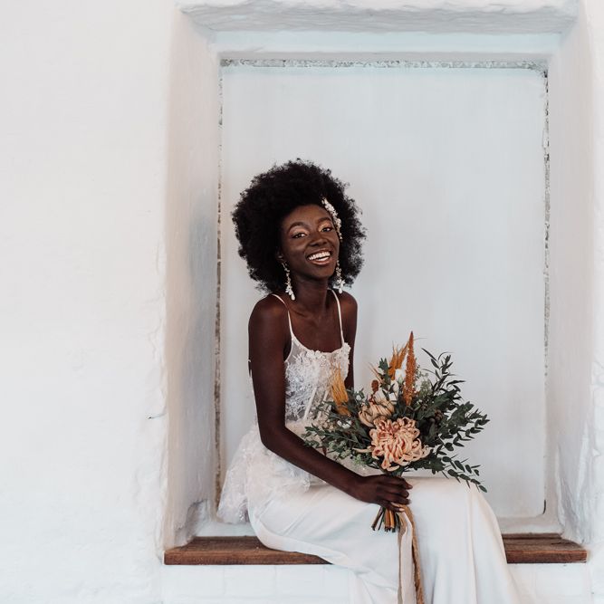 Beautiful bride in a fitted wedding dress with lace peplum bodice sitting in an alcove at Ponden Mill 