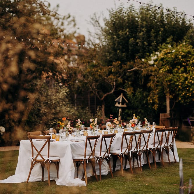 Garden party wedding reception with wooden table and chairs and coloured glass goblets 