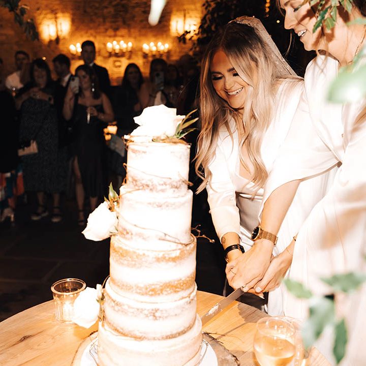 Brides cut naked cake as wedding guests watch on