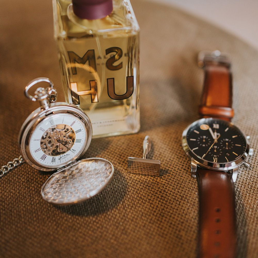 Groom's Jo Malone cologne, pocket watch, cufflink and watch laid out before Tythe Barn wedding with barn wedding flowers