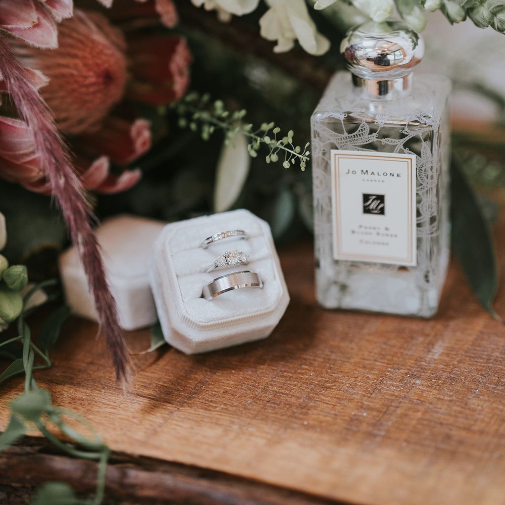 Jo Malone perfume bottle, three silver rings in white box and bridal bouquet with white florals and pink protea at Tythe Barn wedding with barn wedding flowers