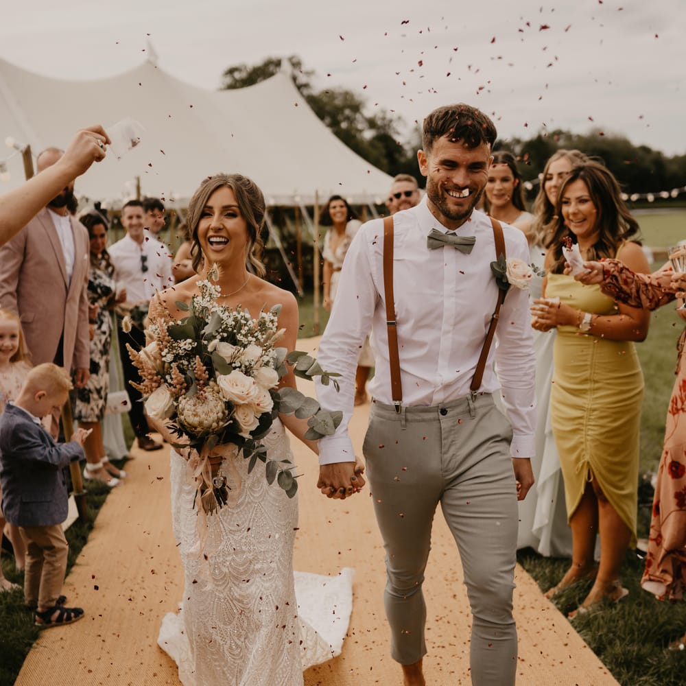 Bride & groom walk through confetti as guests throw confetti around them | Mark Bamforth Photography