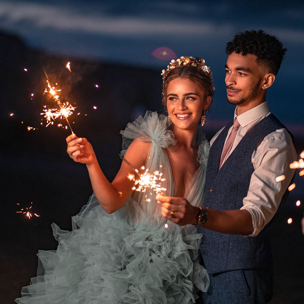 Sparkler moment on the beach with bride in a coloured frilly wedding dress and groom a wool waistcoat 
