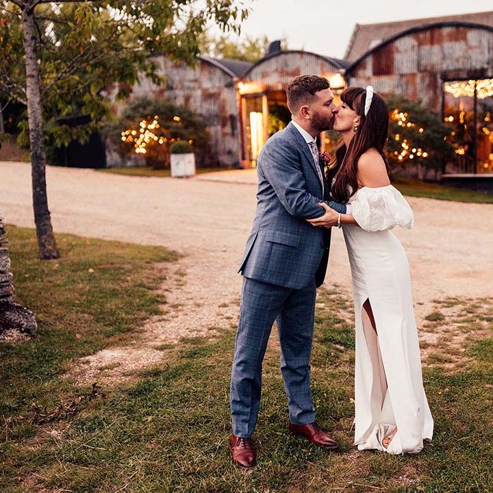 Bride & groom kiss in front of the Stone Barn Cotswolds on their wedding day
