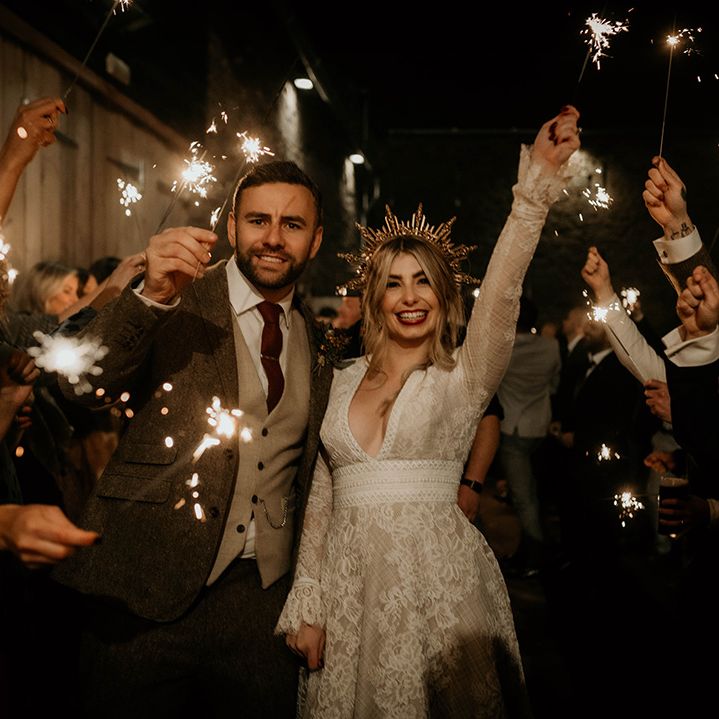 Sparkler moment with bride in a lace wedding dress and gold crown and groom in a tweed suit at Lyde Court 