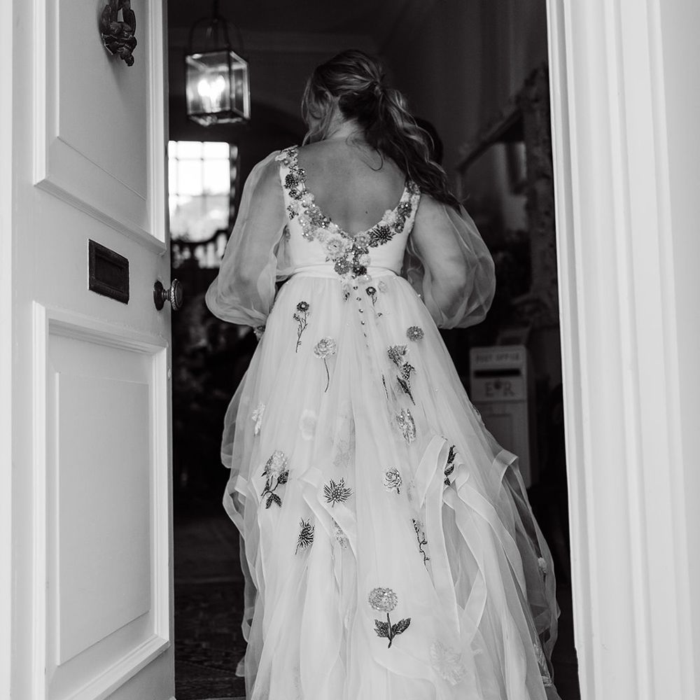 Bride with ponytail and low back wedding dress with tulle train and floral embroidery walks through door at Iscoyd Park