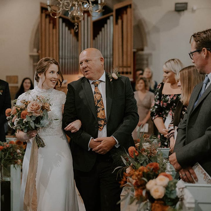 Bride walks down the aisle lined with orange flowers clutching bouquet