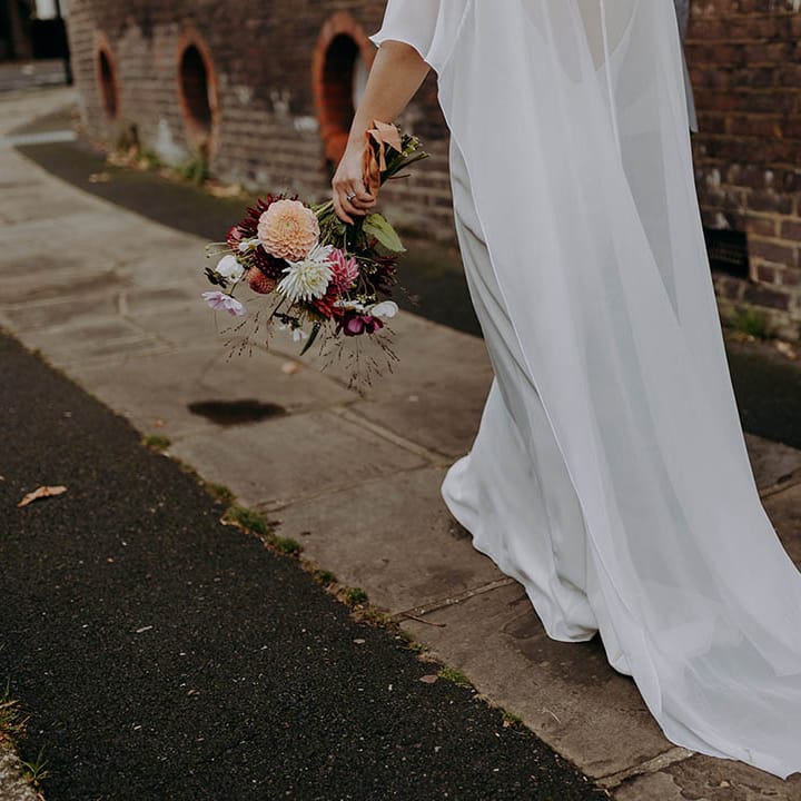 Bride walks down the road wearing sample wedding dress with cape 