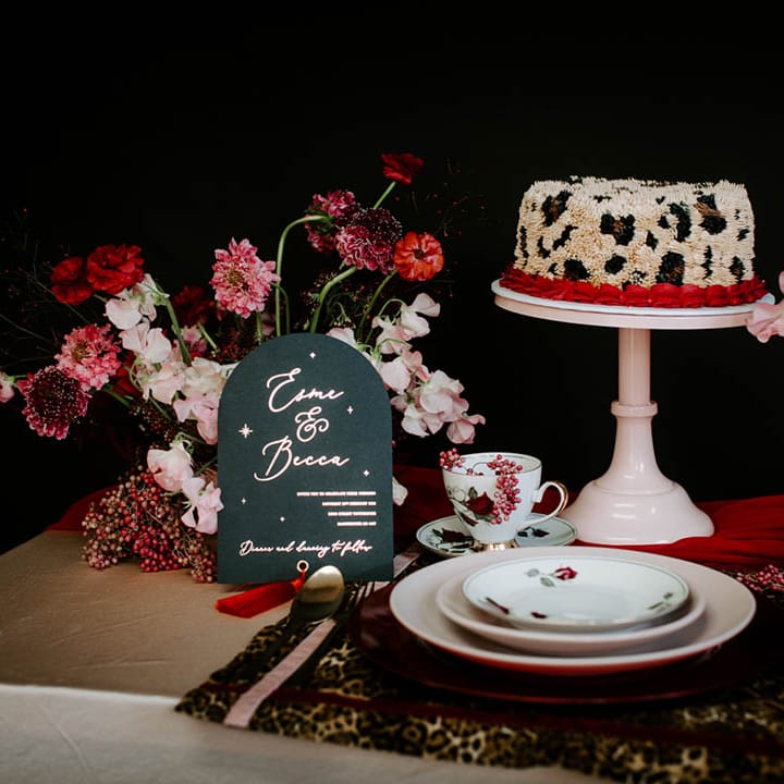 Place setting with gold table cloth, leopard print place matt, black and gold wedding stationery and leopard print buttercream wedding cake 