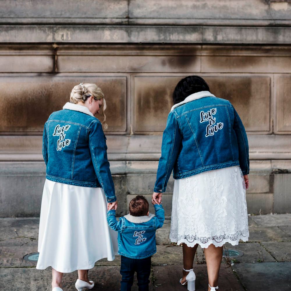 Two brides in tea length wedding dresses and customised denim jackets with their son at their Liverpool Town hall wedding 