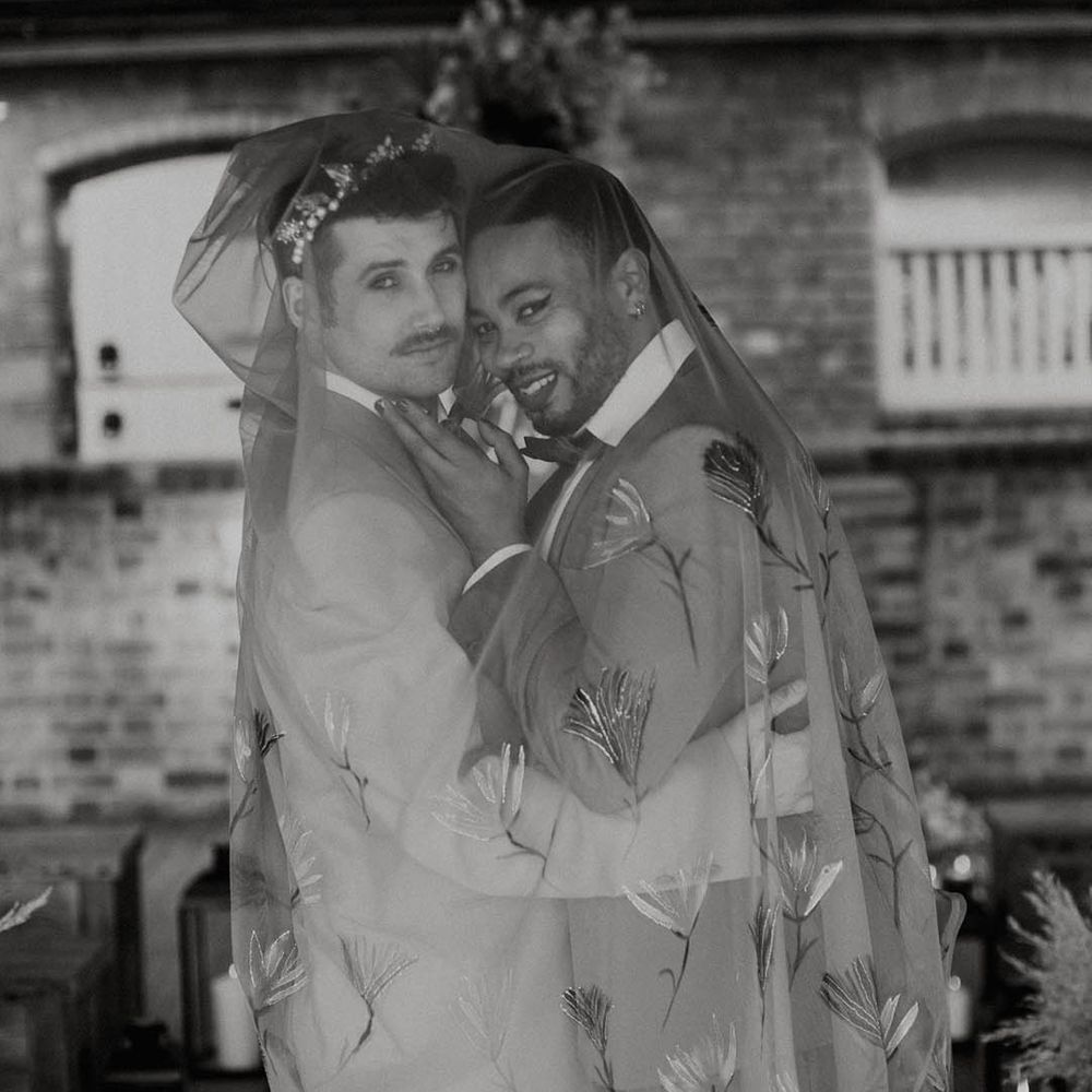LGBTQI+ couple embracing under and embroidered veil 