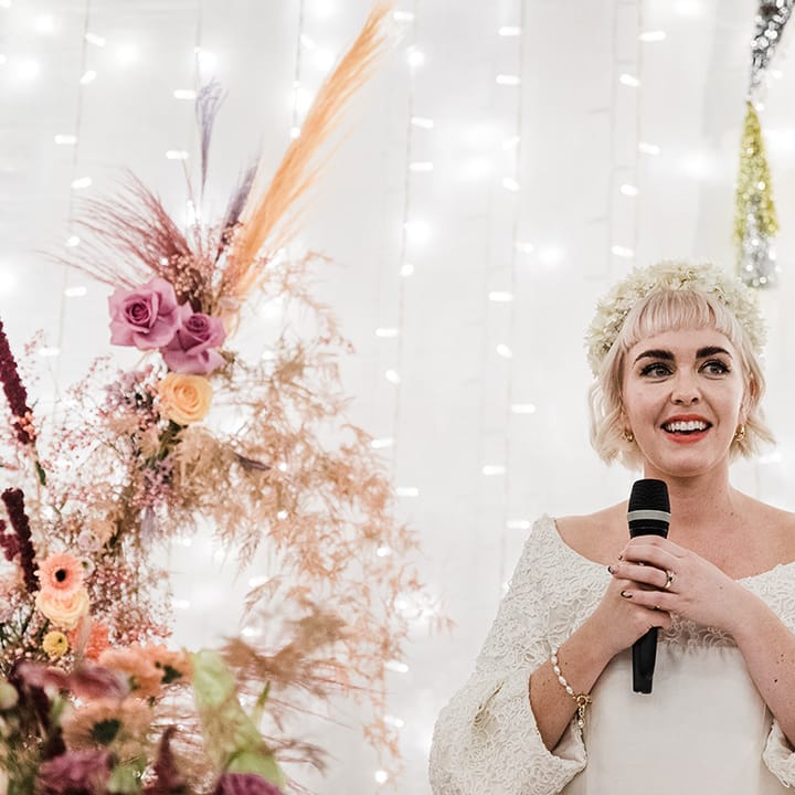 Bride wearing white flower headband and  pearl bracelet gives a bridal speech at her wedding