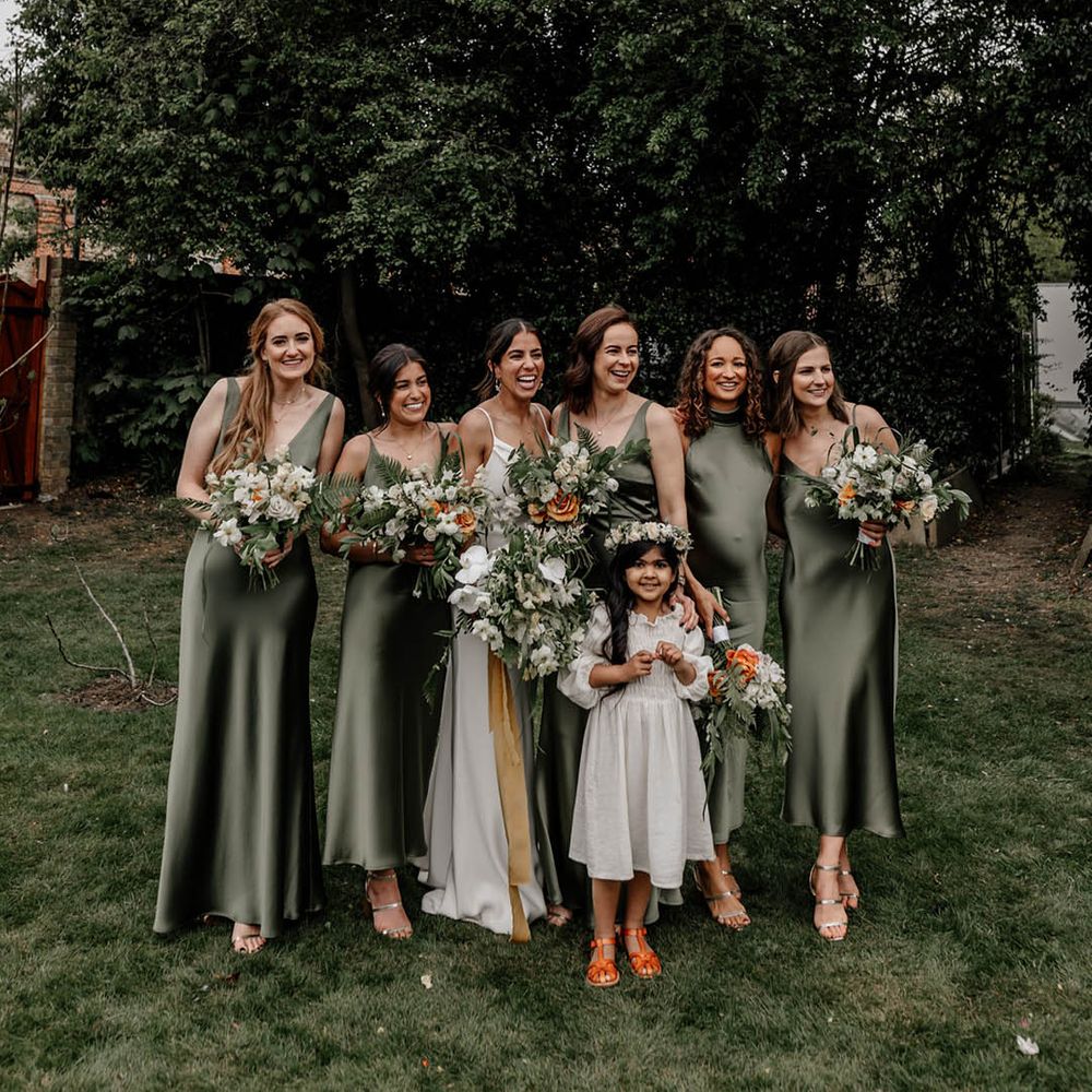 Bridal party in satin sage green bridesmaids dresses and the flower girl wearing a white dress and flower crown