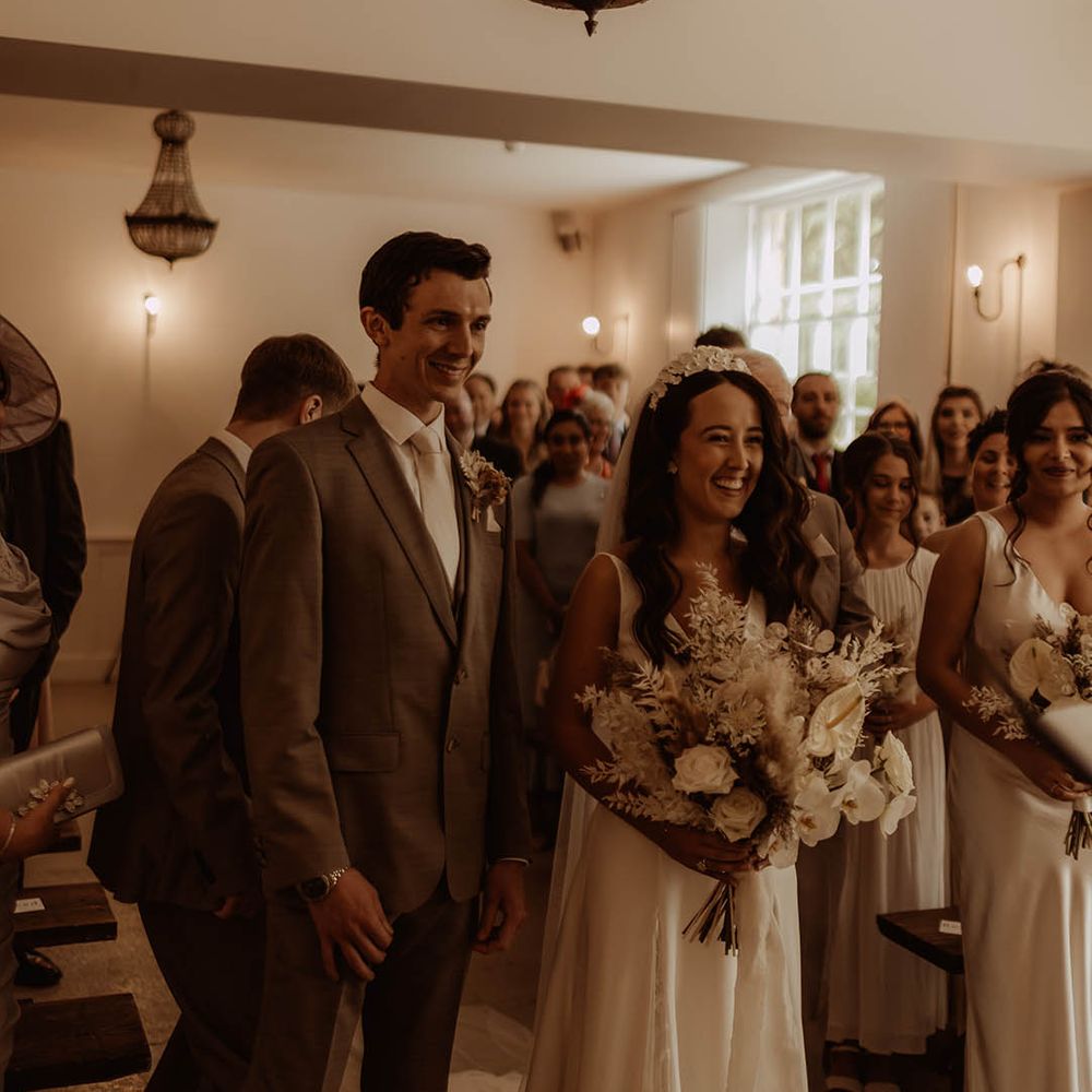Bride in flower bridal headband smiles with the groom in neutral three piece suit for their boho luxe wedding 