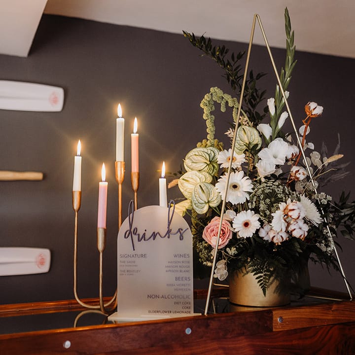 Colourful candles inna gold candle holder with a drinks menu sign and pretty florals 