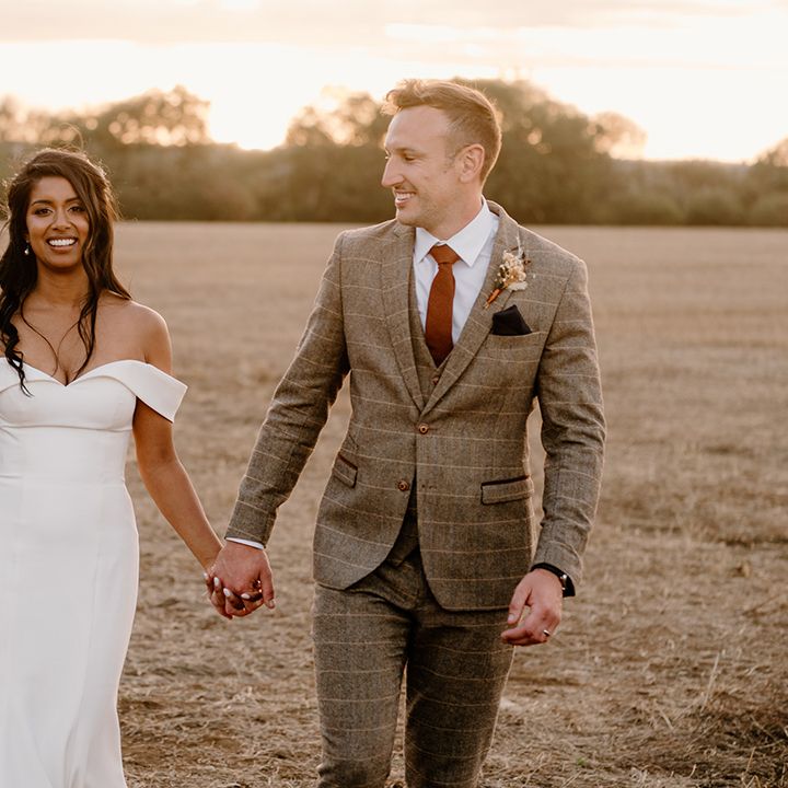 Bride and groom walk holding hands during sunset 