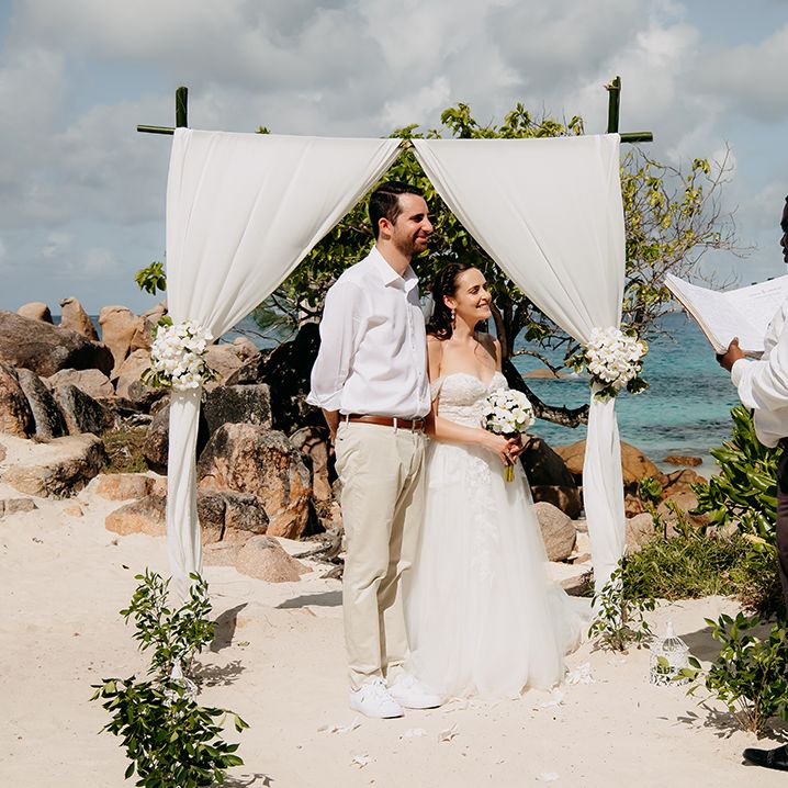 Bride and groom eloping on beach at Praslin Island, Seychelles with chiffon white wedding arch with white tropical flower decorations 