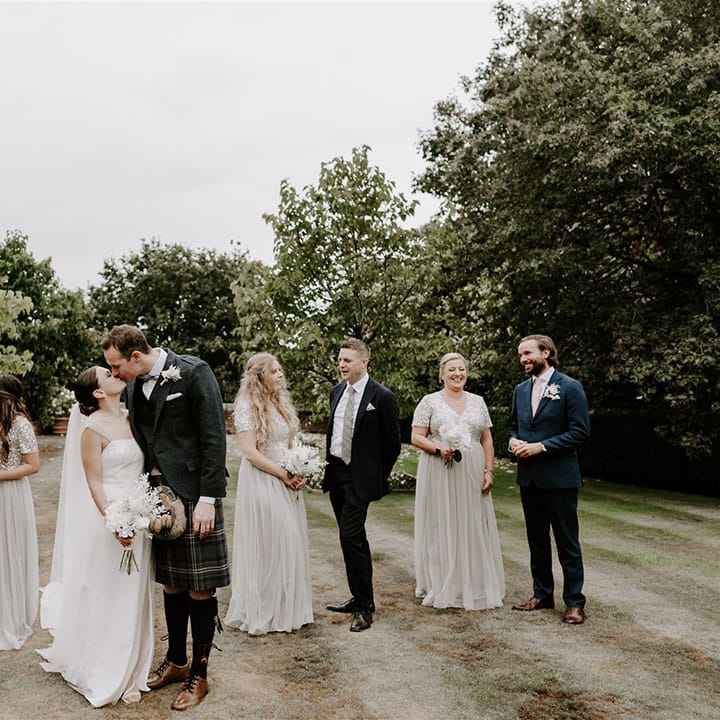 Wedding party shot of the bride and groom kissing with their bridesmaids and groomsmen 