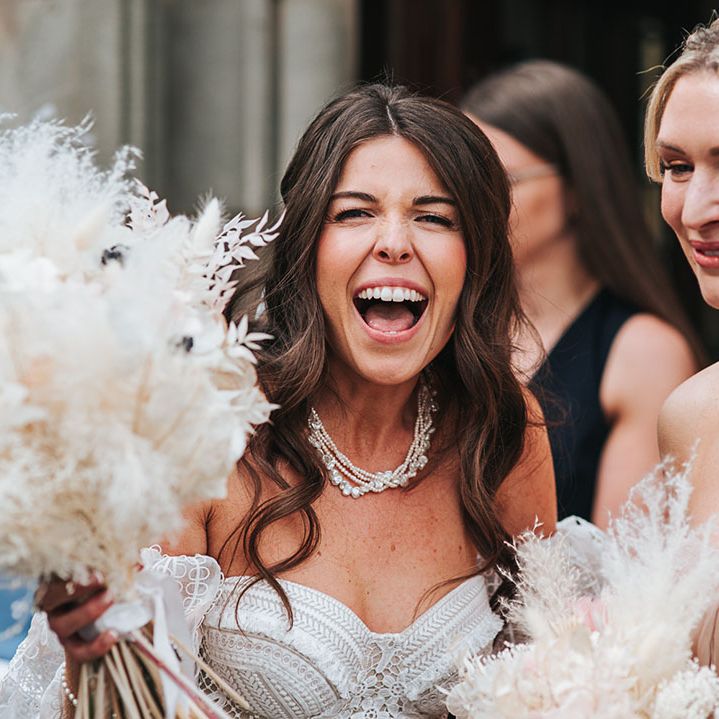 Bride with curled brown hair wearing a pearl necklace in a boho lace strapless gown and dried grass and flower bouquet 
