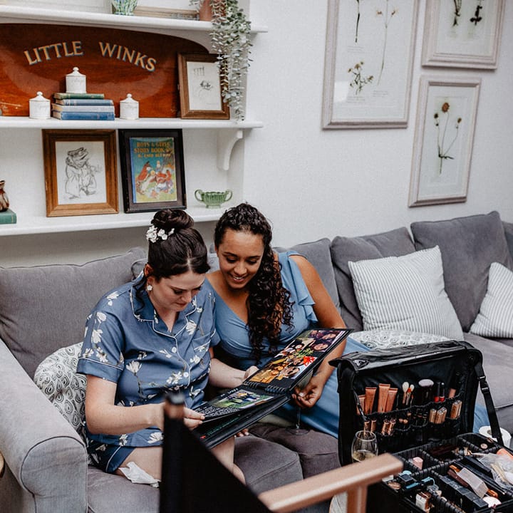 The bride in a blue and flower pyjama set looking through a photo book gifted to the bride from the bridesmaids 