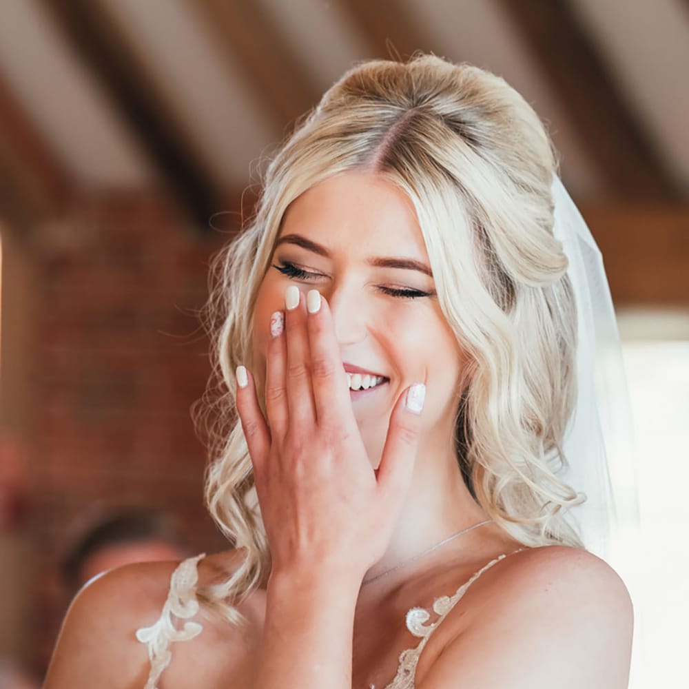 Laughing bride with white wedding nails with pink flower nail art wearing a lace wedding dress and veil 