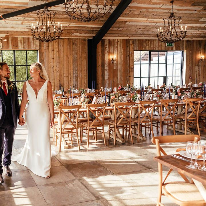 Bride in fitted wedding dress with the groom in a three piece blue suit walking around the wedding reception decorated with blue and orange decor 