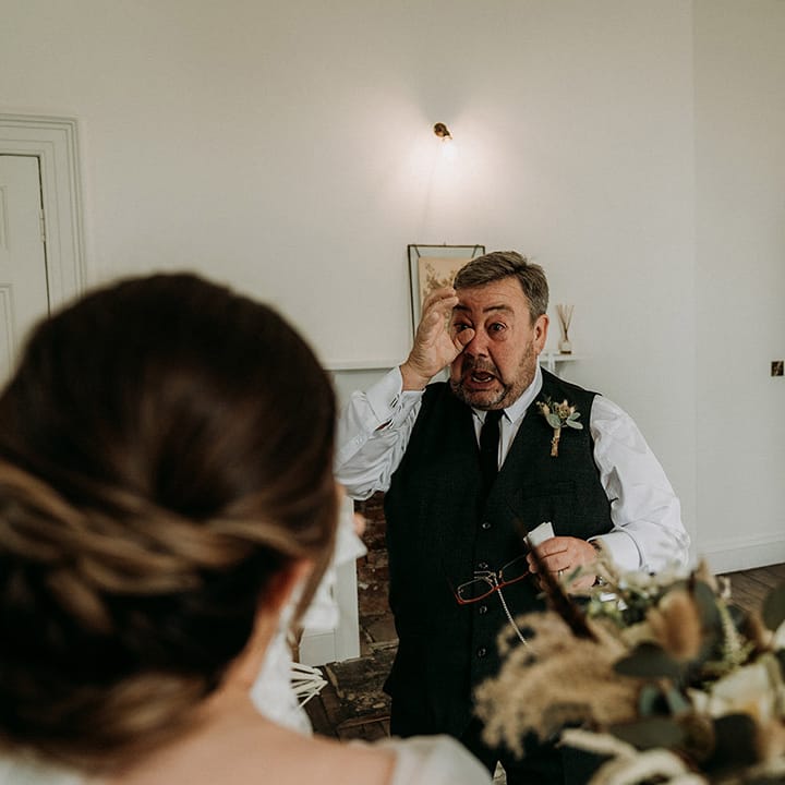 Father of the bride gets emotional and wipes his tears as he sees the bride for the first time in her wedding dress 