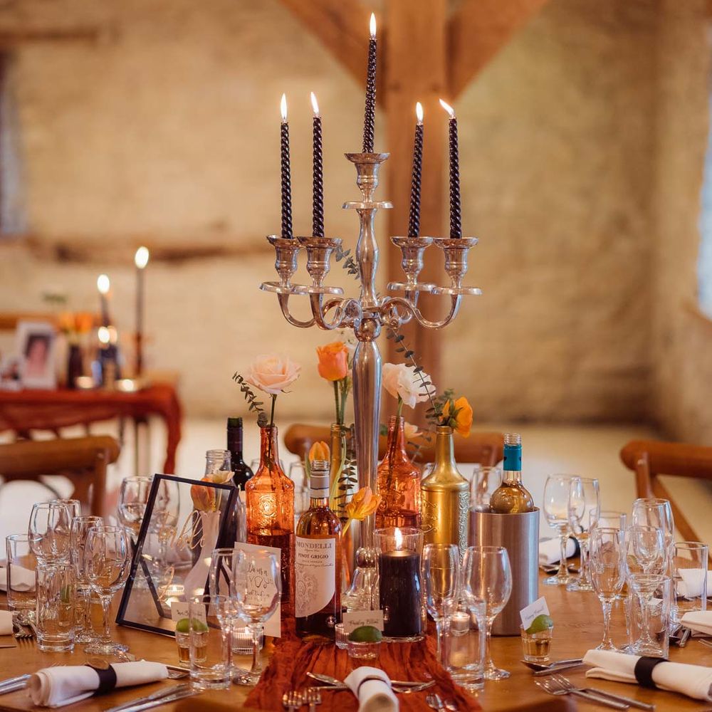 Golden candelabras with black polka dot tapered candles on rust orange wedding tablescape at Kingscote Barn Tetbury wedding venue with fairy lights and festoon lighting 