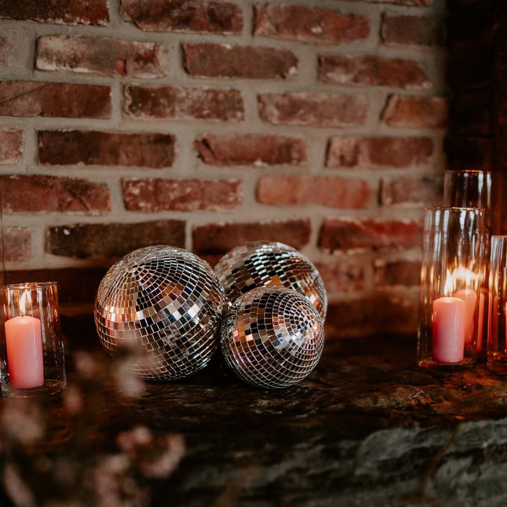 Disco ball wedding decorations with pink tapered candles in tall glass candle jars on top of exposed brick fireplace at Willow Marsh Farm Loughborough 