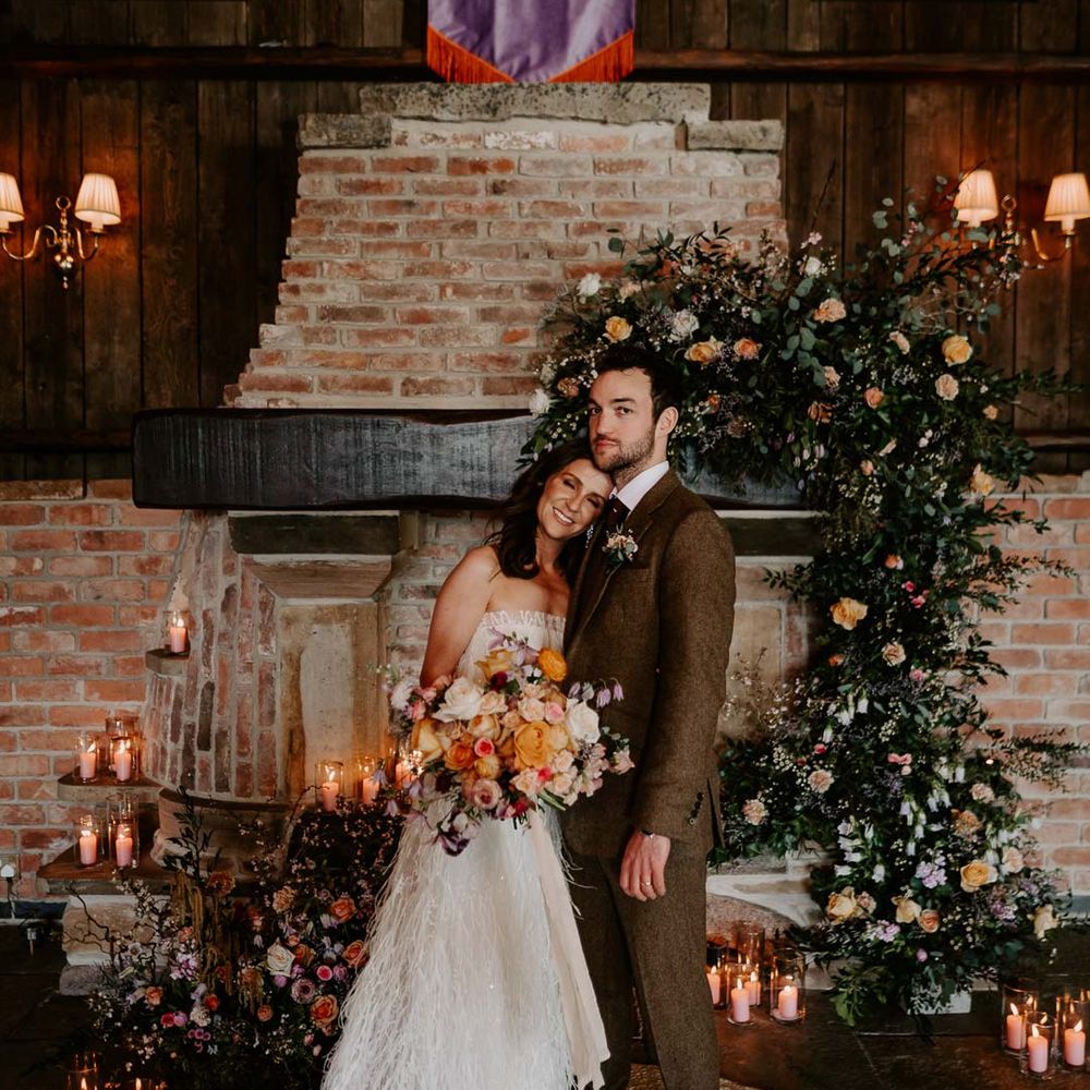Bride in strapless ivory fringed crepe gown and chapel length veil holding large mixed bridal bouquet with garden roses, carnations, peonies and foliage standing with groom in chocolate brown grooms suit 