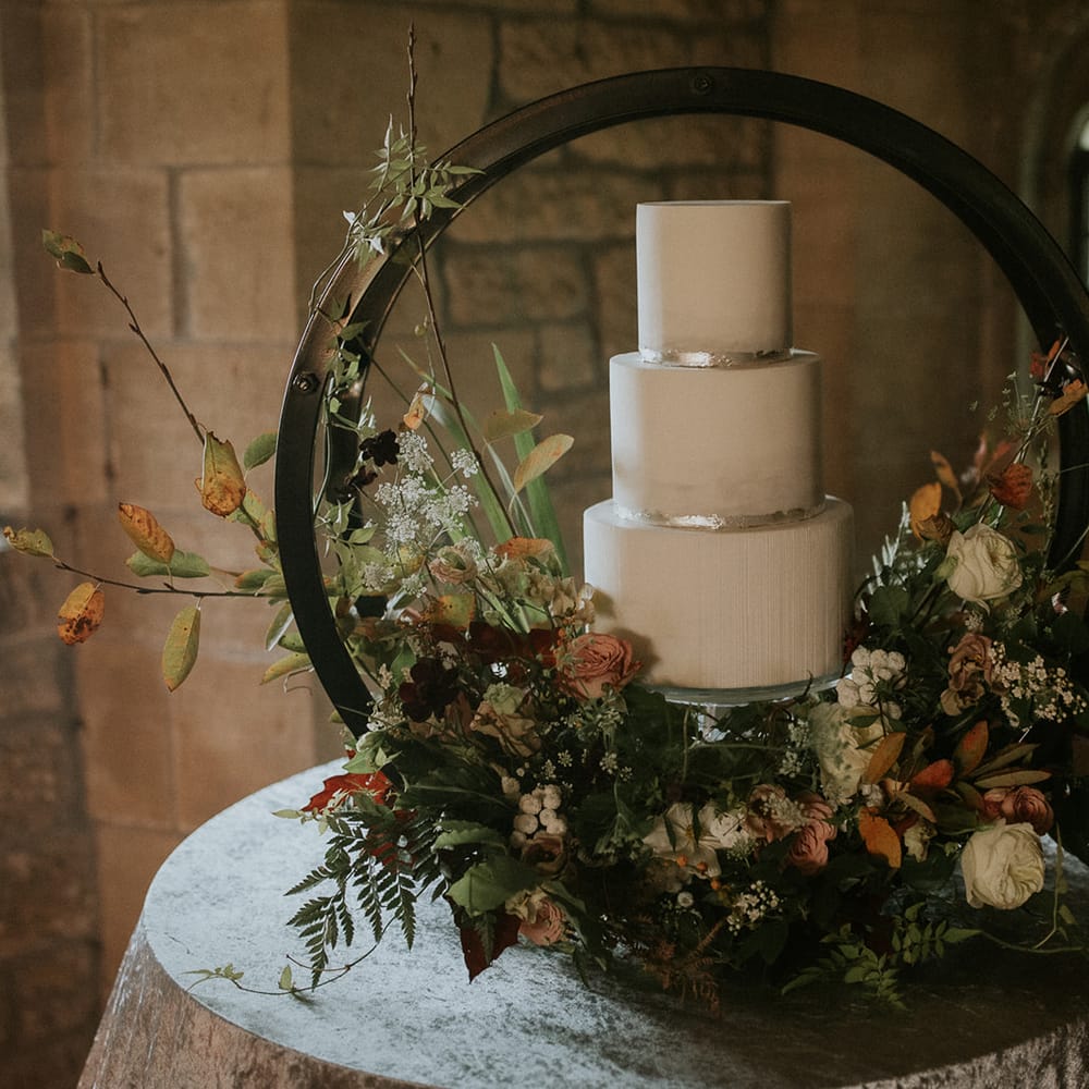 White wedding cake with silver leaf decor on a hoop cake stand decorated with autumn flowers 
