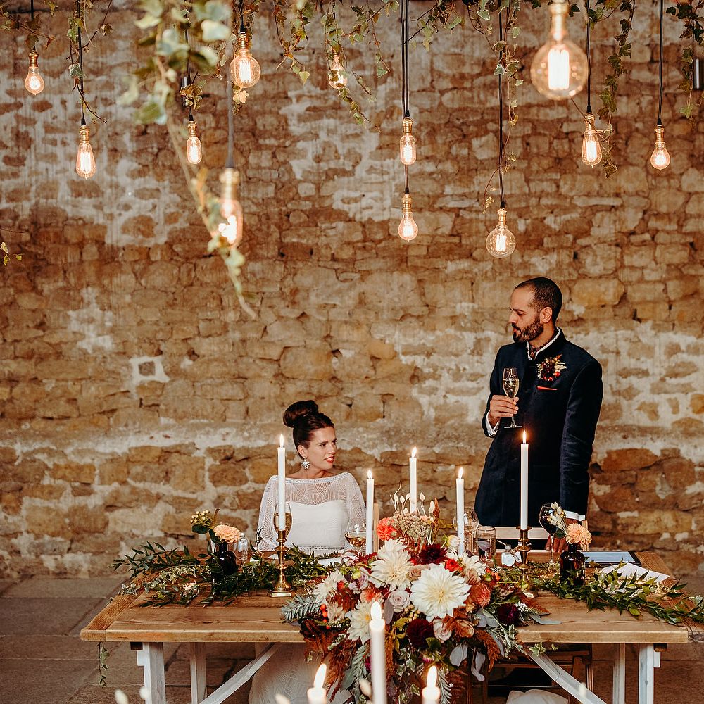 Bride & groom sit together with brick wall background and hanging lights