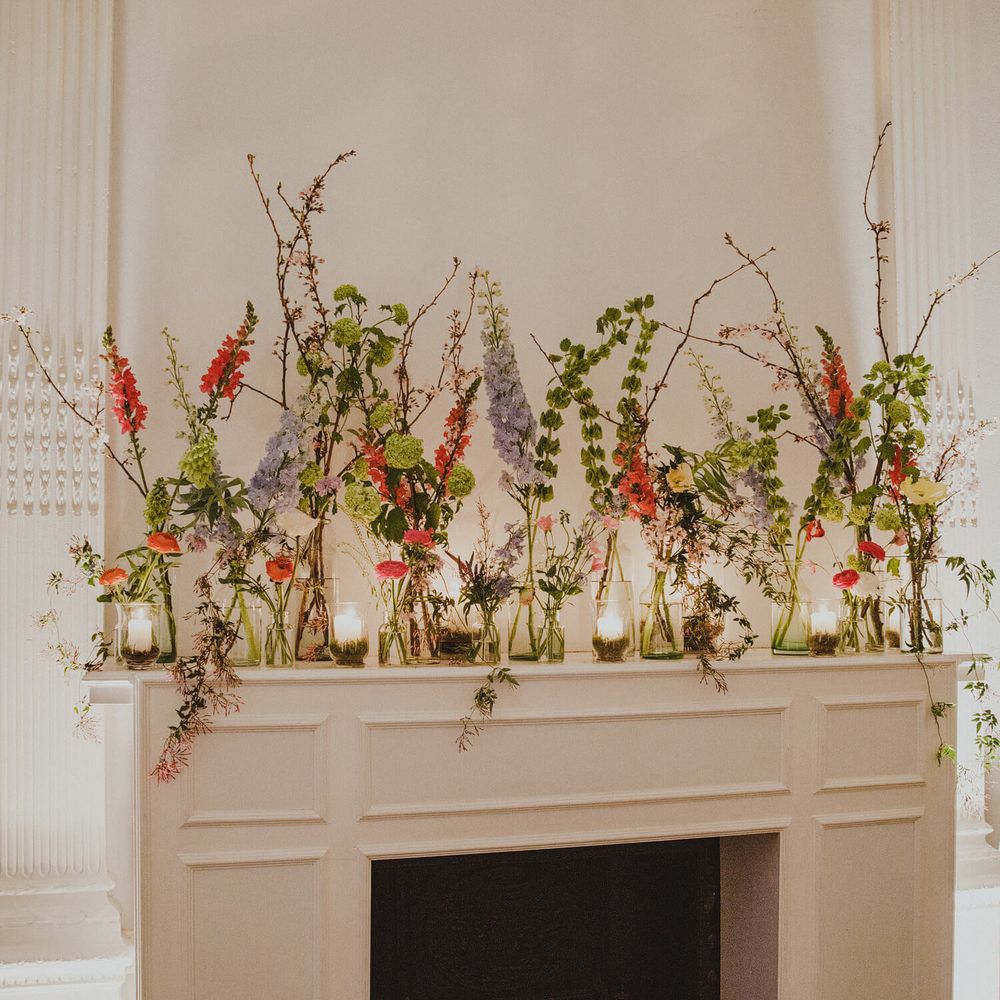Wedding venue mantlepiece decorated with bud vases filled with bright poppies and greenery and candles 