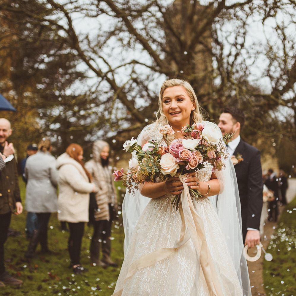 Bride in a princess wedding dress by Enzoani and bespoke bridal cape holding a blush pink wedding bouquet 