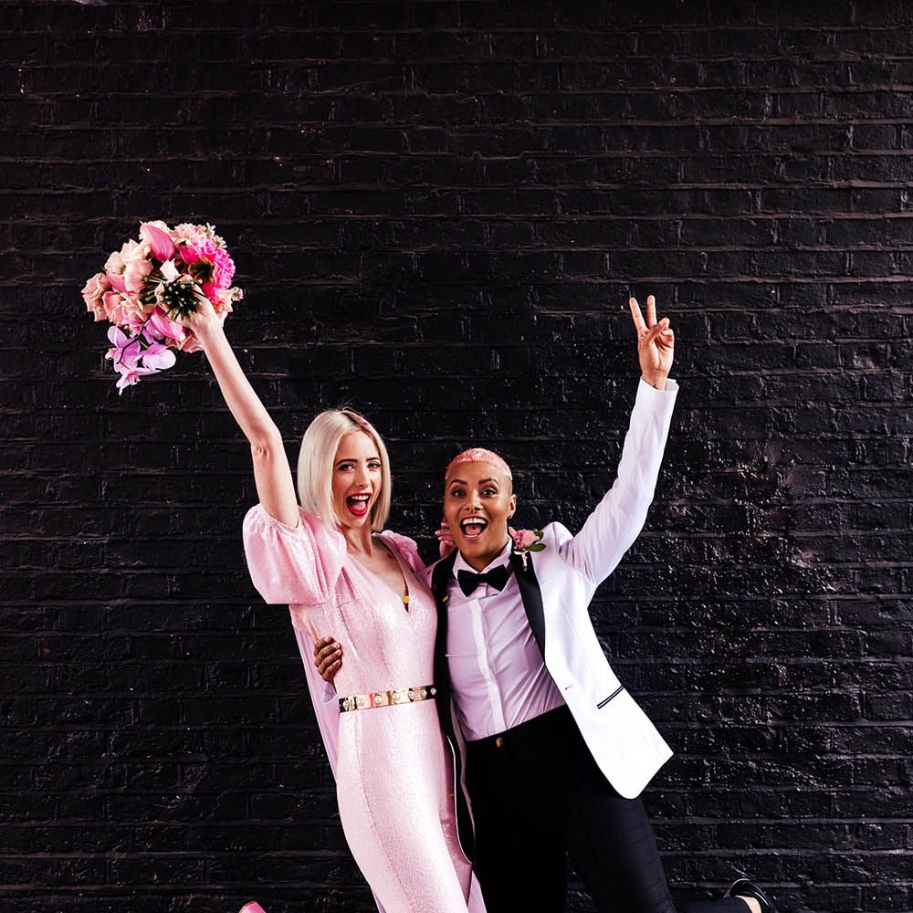 Alternative bride and bride photo with brides in a pink jumpsuit and white tuxedo jacket 