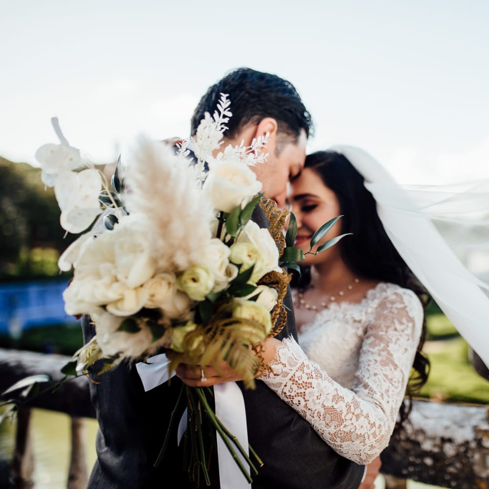 Groom holds out brides classic bouquet as her veil blows in the wind