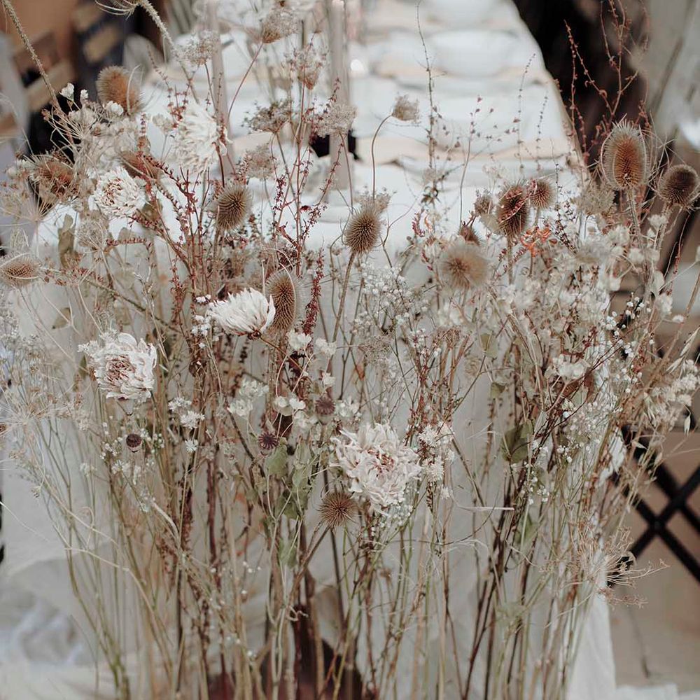 Tall dried flower stems in a wooden stand at the end of the wedding reception table 