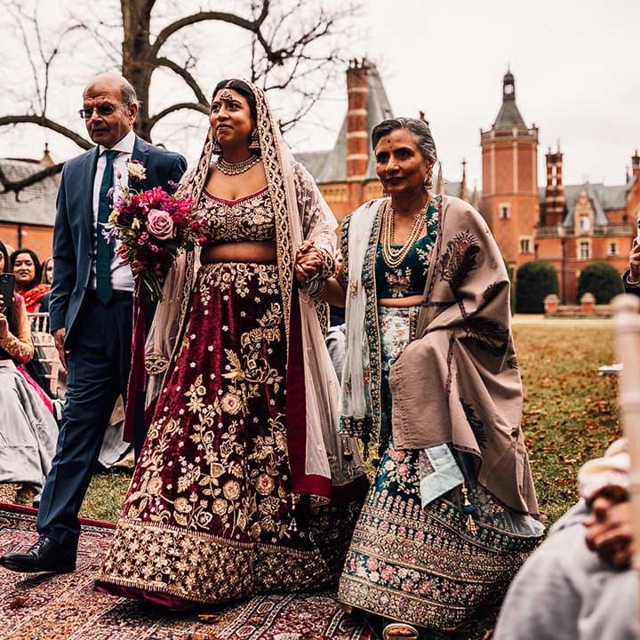 Mother and Father hold their daughters arm walking her down the aisle 