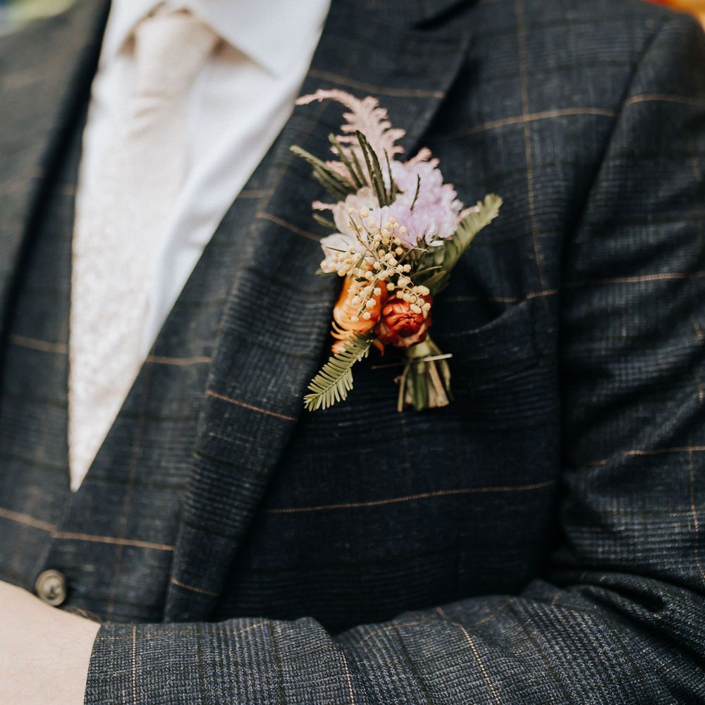 Groom in check suit three piece suit and pink tie wears purple and orange floral buttonhole